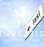 White signboard with an arrow pointing left towards Iasi, Romania, against a hazy blue sky in a concept of travel, navigation and direction. Path included for the signboard
